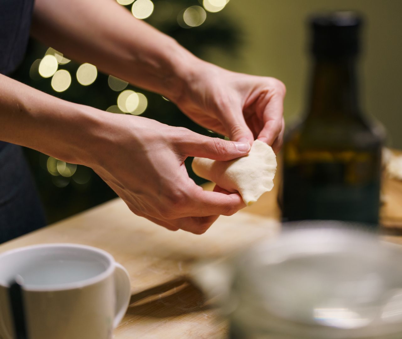 Hands crafting dumplings in a cozy kitchen setting with warm festive lights. Perfect for holiday cuisine.